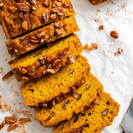 A partially sliced loaf of cinnamon sugar pumpkin bread on white parchment paper.