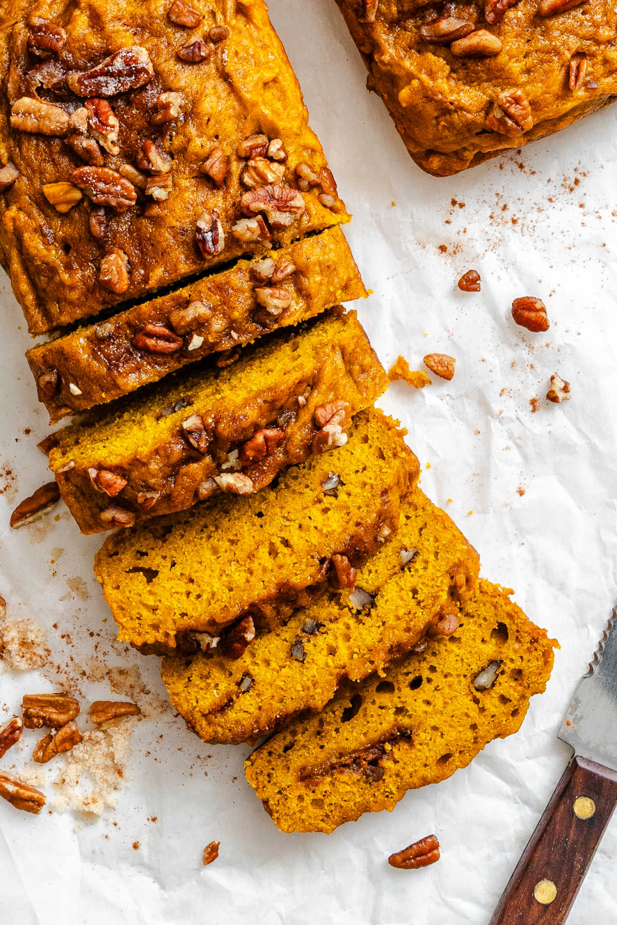 Cinnamon Sugar Pumpkin Bread A partially sliced loaf of cinnamon sugar pumpkin bread on white parchment paper.