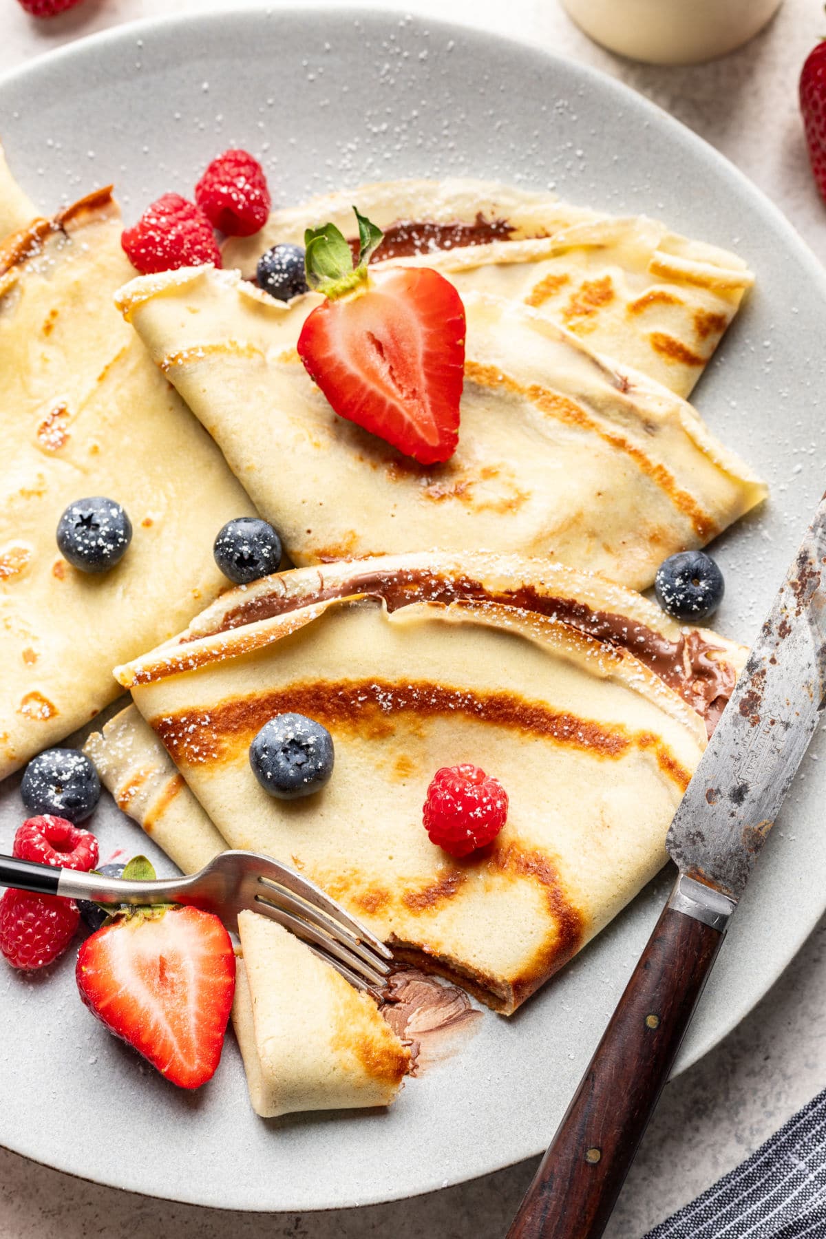 A fork taking a bite of a Nutella filled crepe topped with fresh berries.