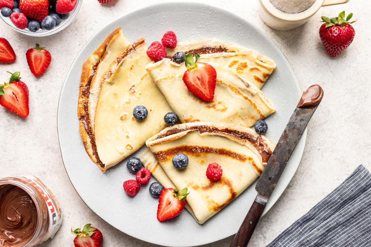 A plate of crepes with various fillings next to a dish of fresh berries.