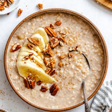 A bowl of crock pot banana bread oatmeal in a dish topped with sliced banana and pecans.