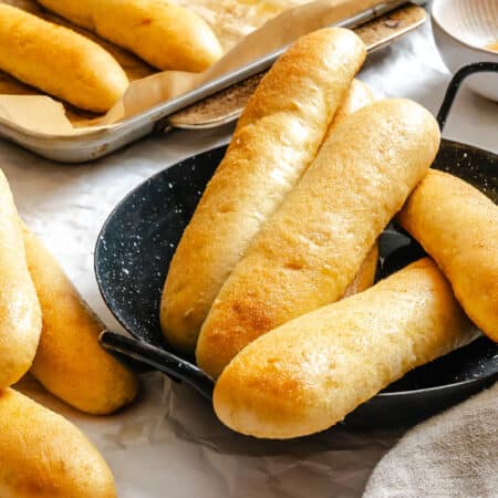 Garlic breadsticks in stacks next to a plate of breadsticks.