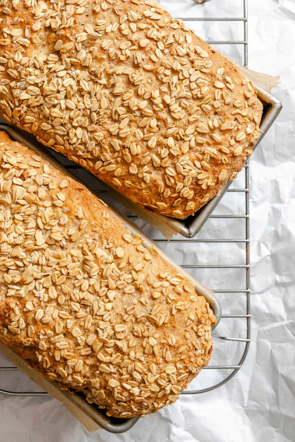 Multigrain Bread Recipe Two loaves of multigrain bread in pans on a cooling rack.