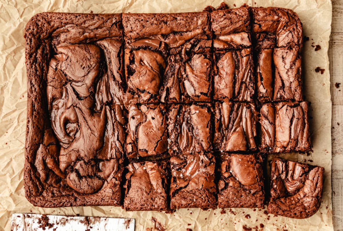 Moule de brownies au Nutella partiellement découpé sur du papier sulfurisé.