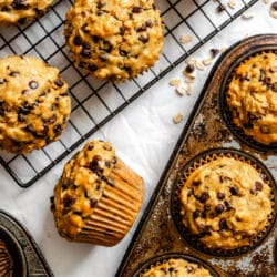 A pan of oatmeal chocolate chip muffins next to a wire cooling rack with muffins on it.