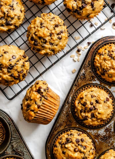 A pan of oatmeal chocolate chip muffins next to a wire cooling rack with muffins on it.