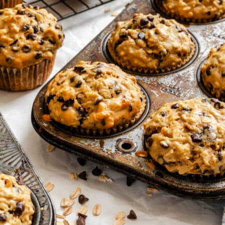 Oatmeal chocolate chip muffins in a muffin pan next to chocolate chips.