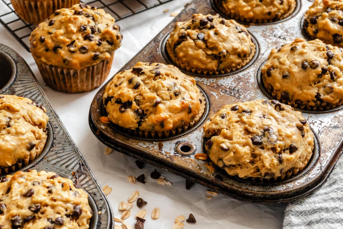 Oatmeal chocolate chip muffins in a muffin pan next to chocolate chips. 