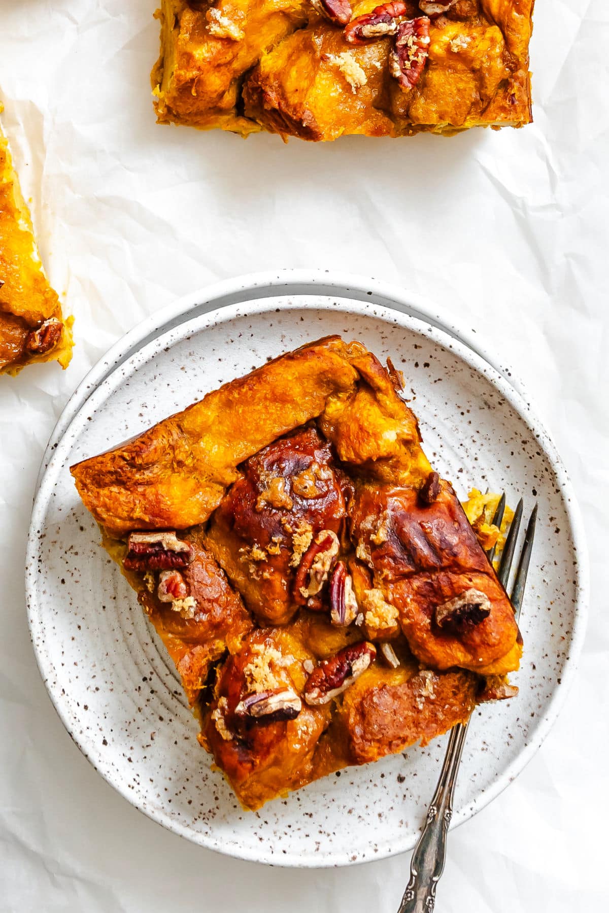 A slice of pumpkin bread pudding on a speckled plate with a fork.