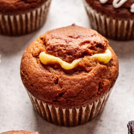 An uniced pumpkin cream cheese muffin next to iced muffins.