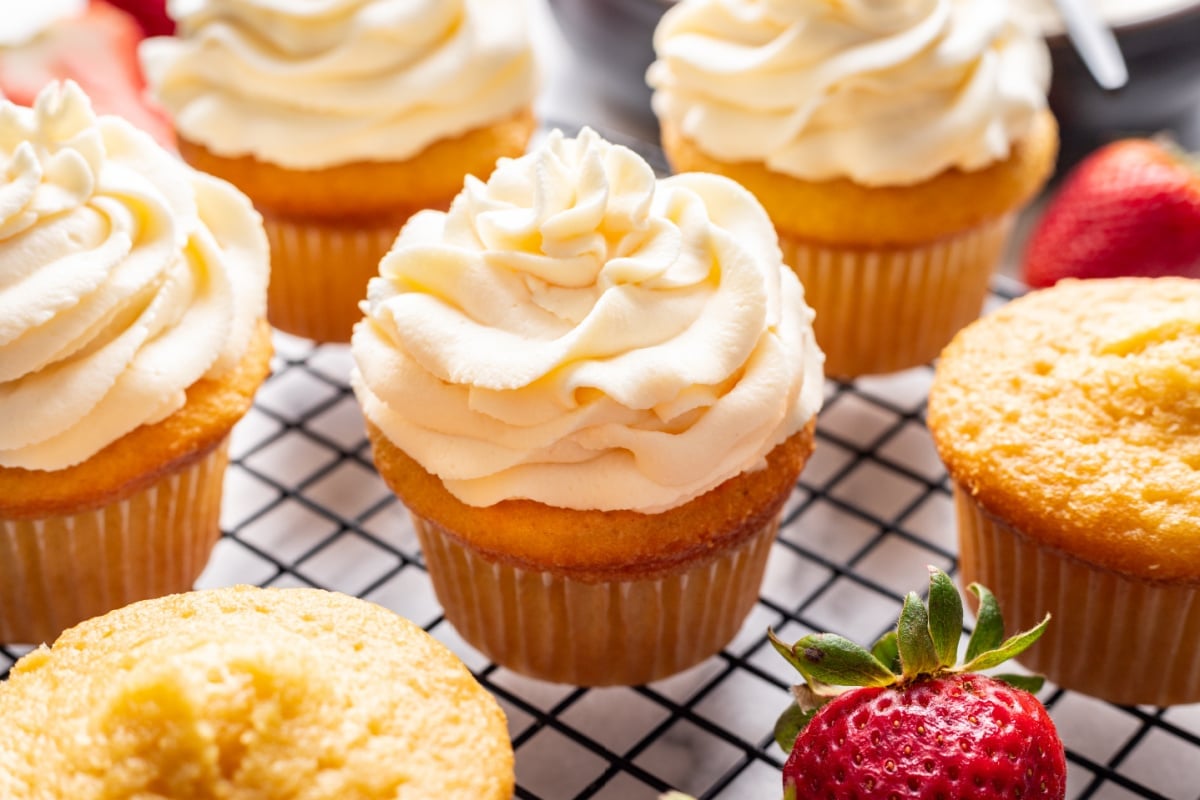 Whipped cream frosting on vanilla cupcakes on a cooling rack.