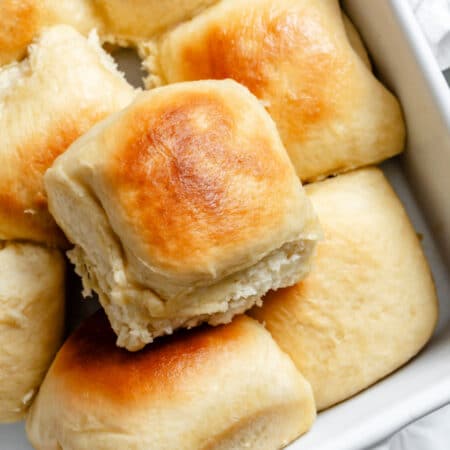 A one hour Hawaiian roll on top of a pan of rolls.