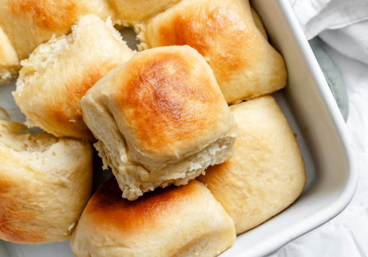 A one hour Hawaiian roll on top of a pan of rolls.
