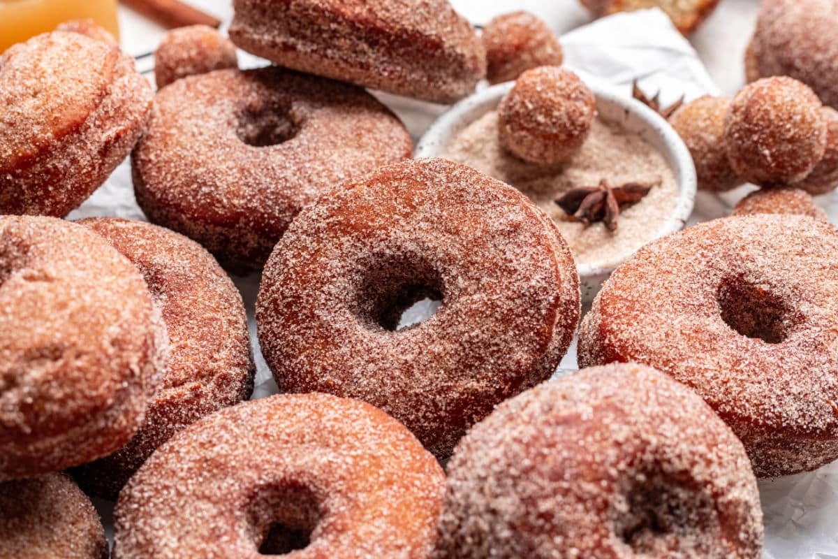 A donut hole and star anise in cinnamon sugar next to apple cider donuts. 