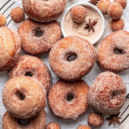 Overlapping apple cider donuts on a parchment lined wire rack.