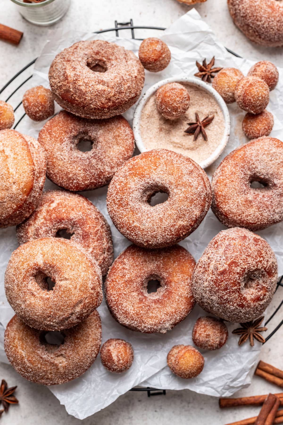 Overlapping apple cider donuts on a parchment lined wire rack.