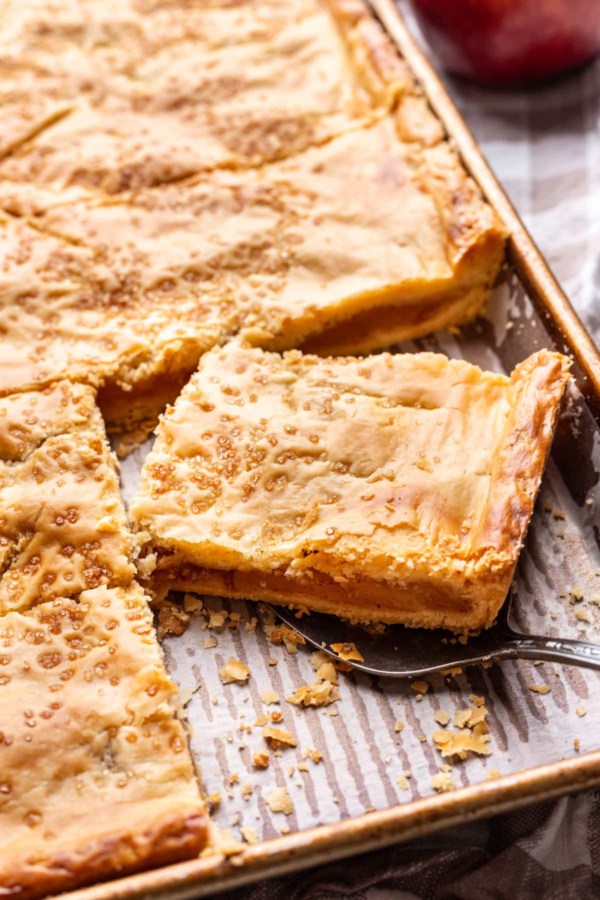 A slice of apple slab pie on a server in the pan.