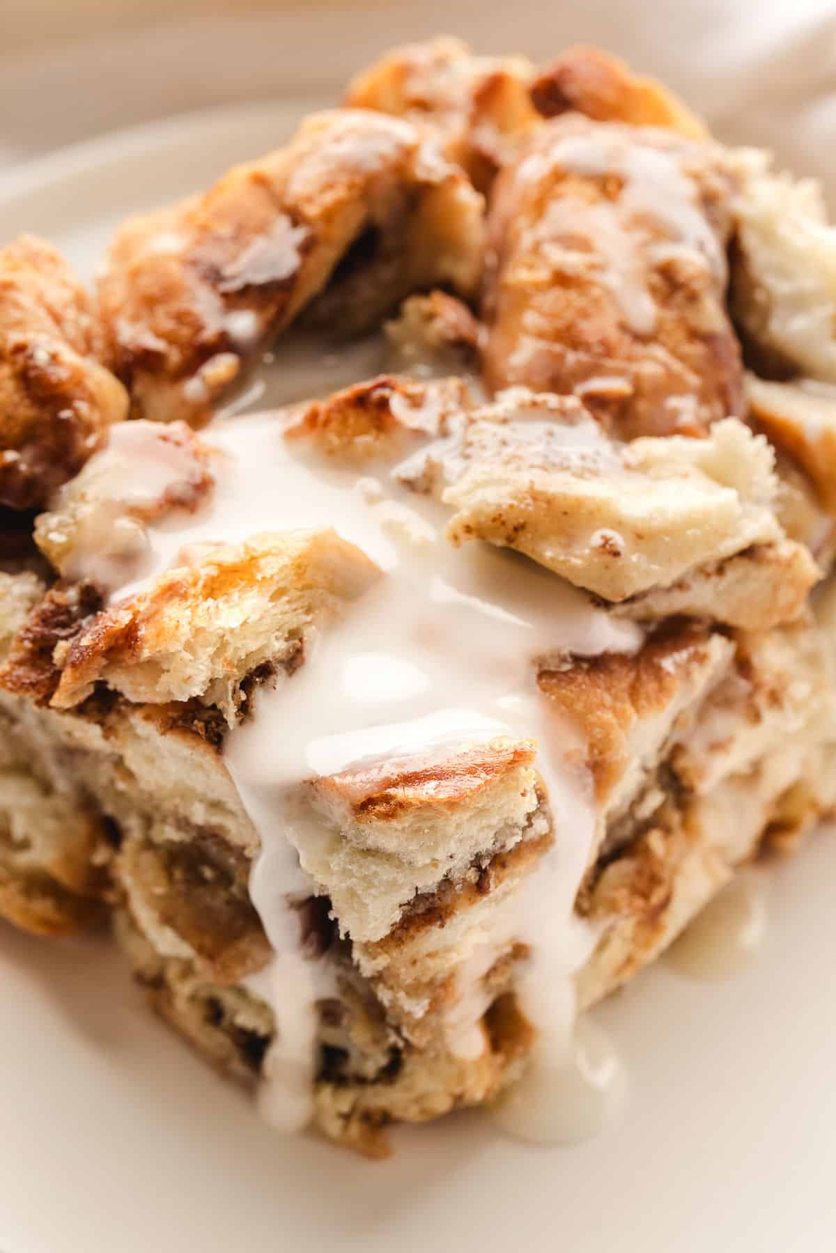 A piece of iced cinnamon roll casserole on a cream plate.