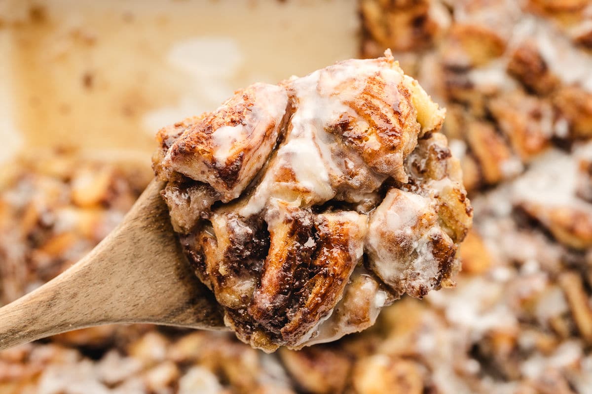 A wooden spoon holding up a scoop of iced cinnamon roll casserole.