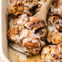 A wooden spoon scooping up cinnamon roll casserole in a baking dish.