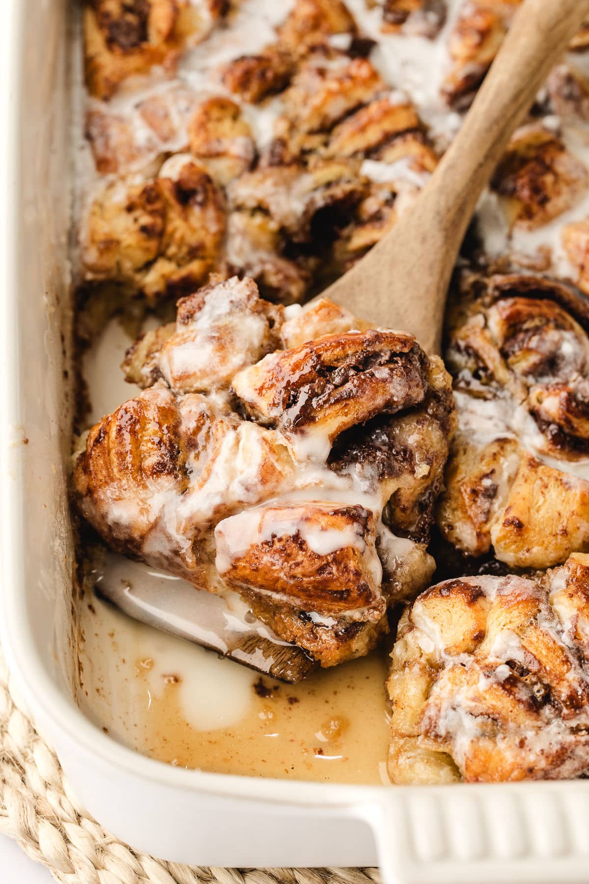 A wooden spoon scooping up cinnamon roll casserole in a baking dish.