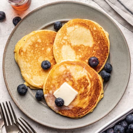 A plate with three corn cakes topped with fresh blueberries and pats of butter.