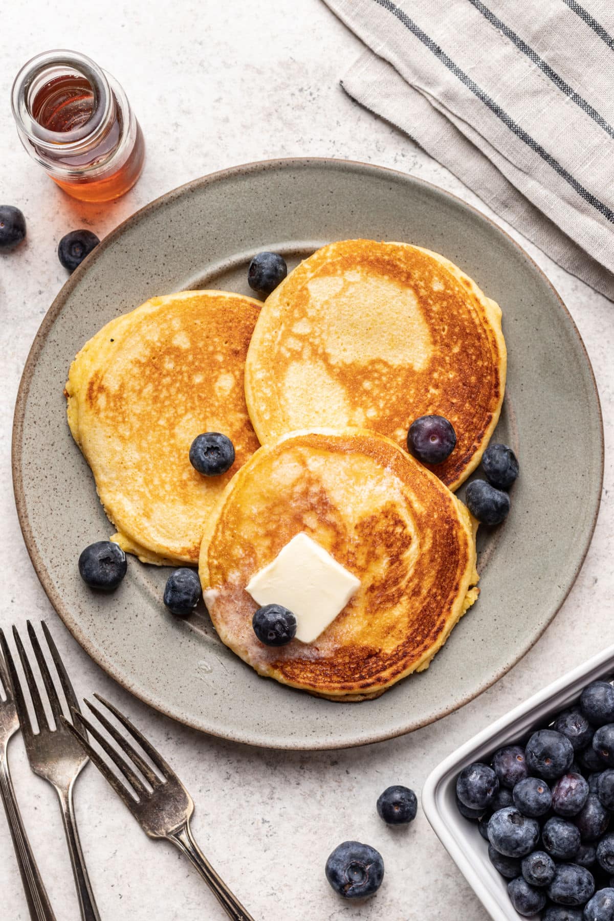 Une assiette avec trois gâteaux de maïs garnis de myrtilles fraîches et de noisettes de beurre.