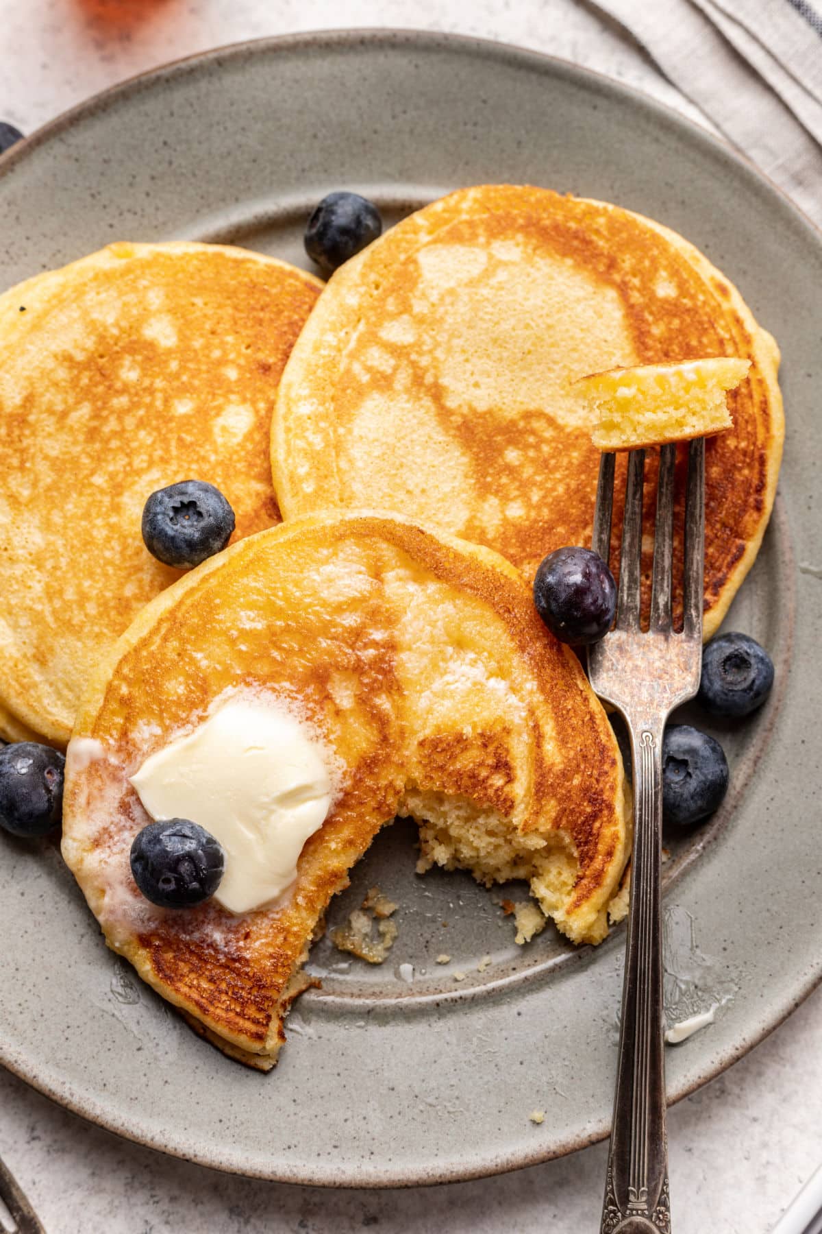 A corncake with a bite missing next to a fork on a plate. 