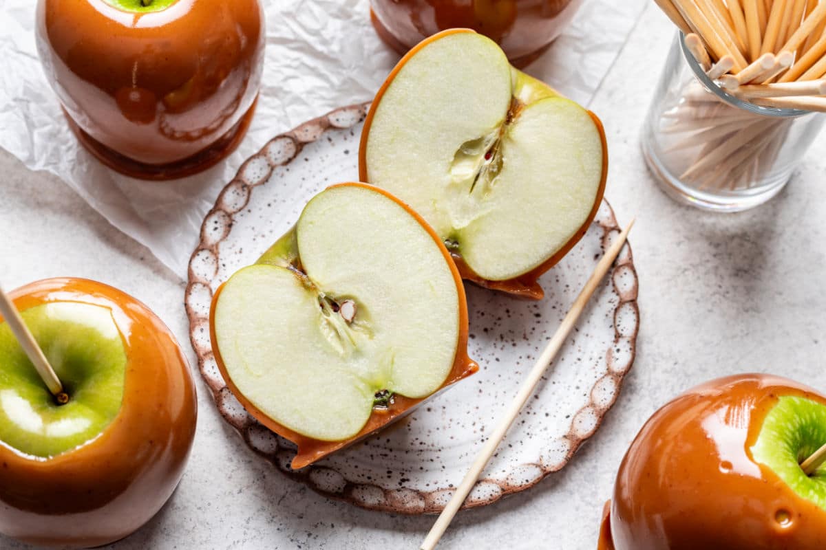 Une pomme au caramel coupée en deux entourée de pommes au caramel.