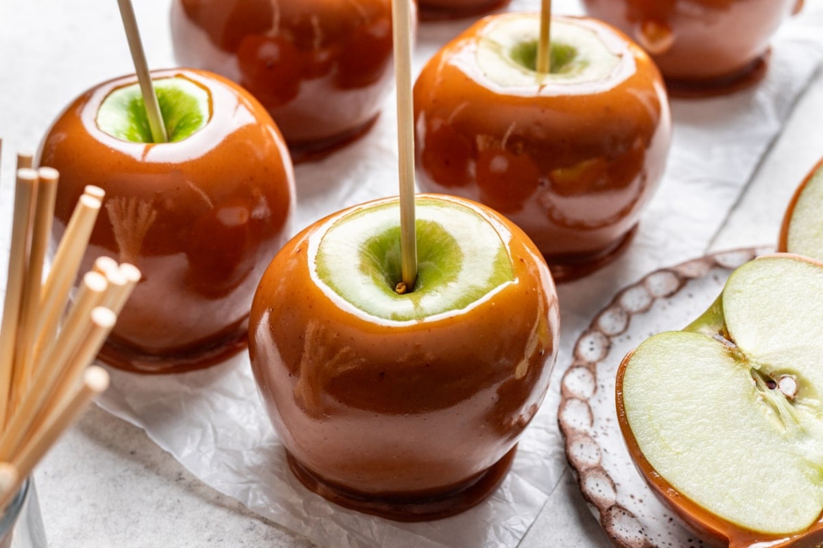 Un plateau de pommes au caramel à côté d'un bocal de brochettes en bois.