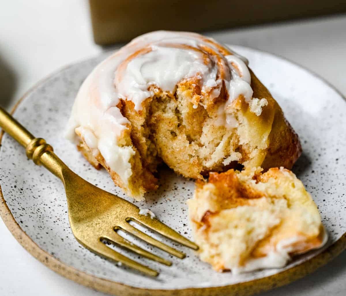 A fork taking a bite of a honey bun on a plate.