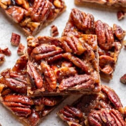 A pecan pie bar on top of other bars next to chopped pecans.
