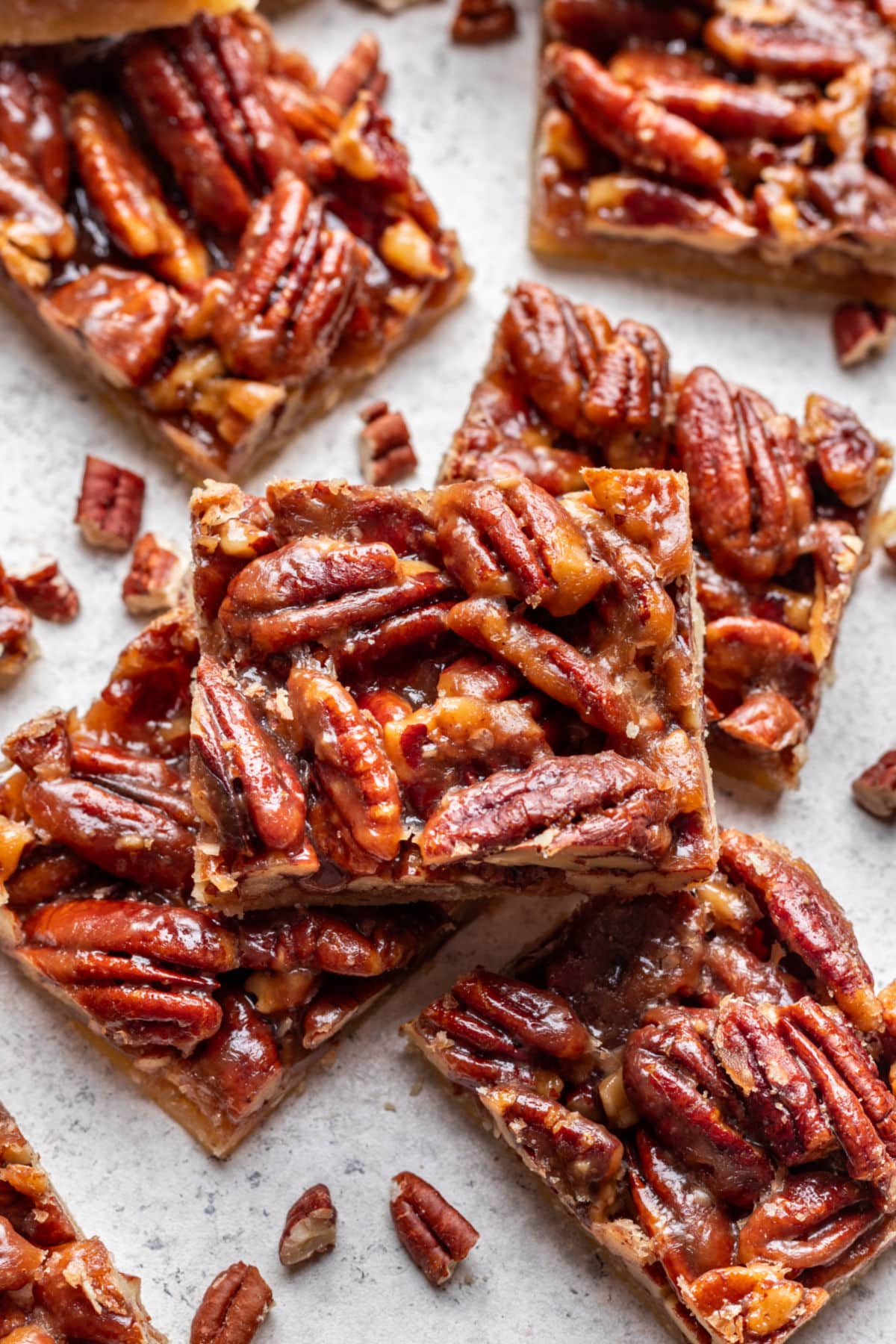 A pecan pie bar on top of other bars next to chopped pecans.