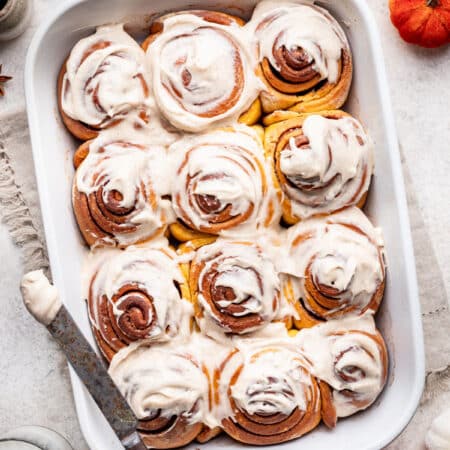 A frosted pumpkin cinnamon rolls in a pan.