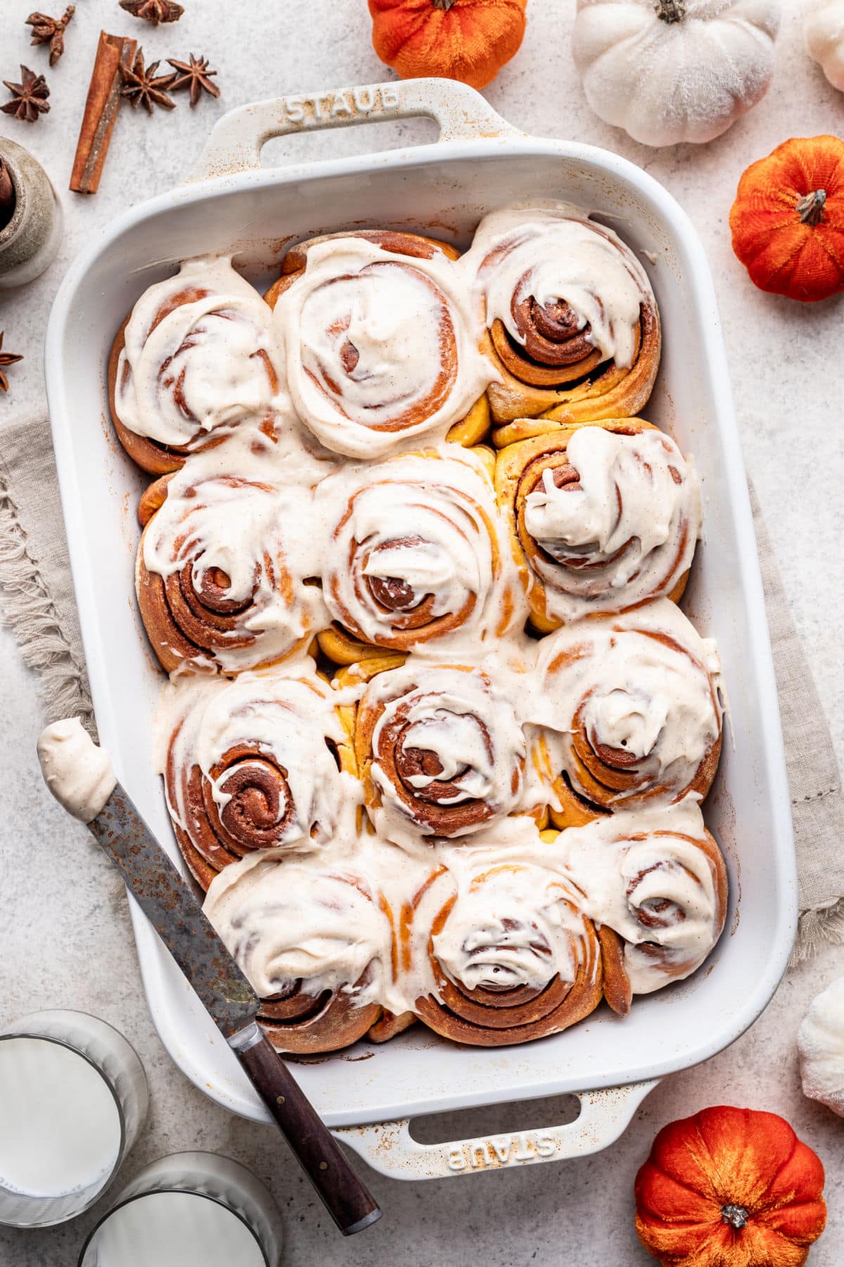 A frosted pumpkin cinnamon rolls in a pan.