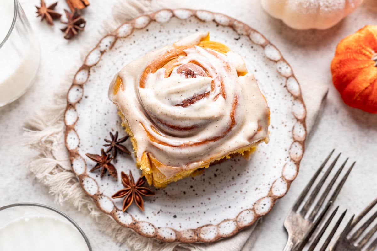 A pumpkin cinnamon roll on a plate next to star anise.