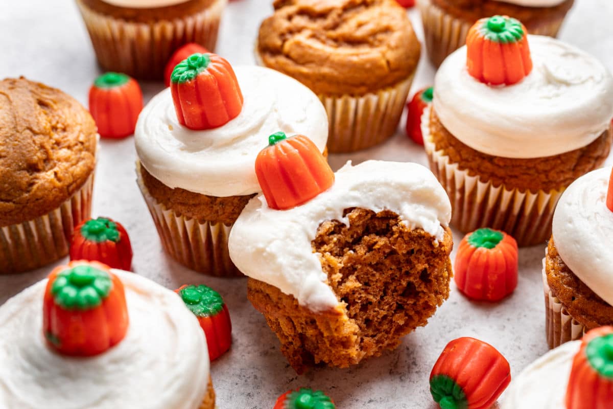A frosted pumpkin cupcake with a bite missing at an angle against another cupcake.