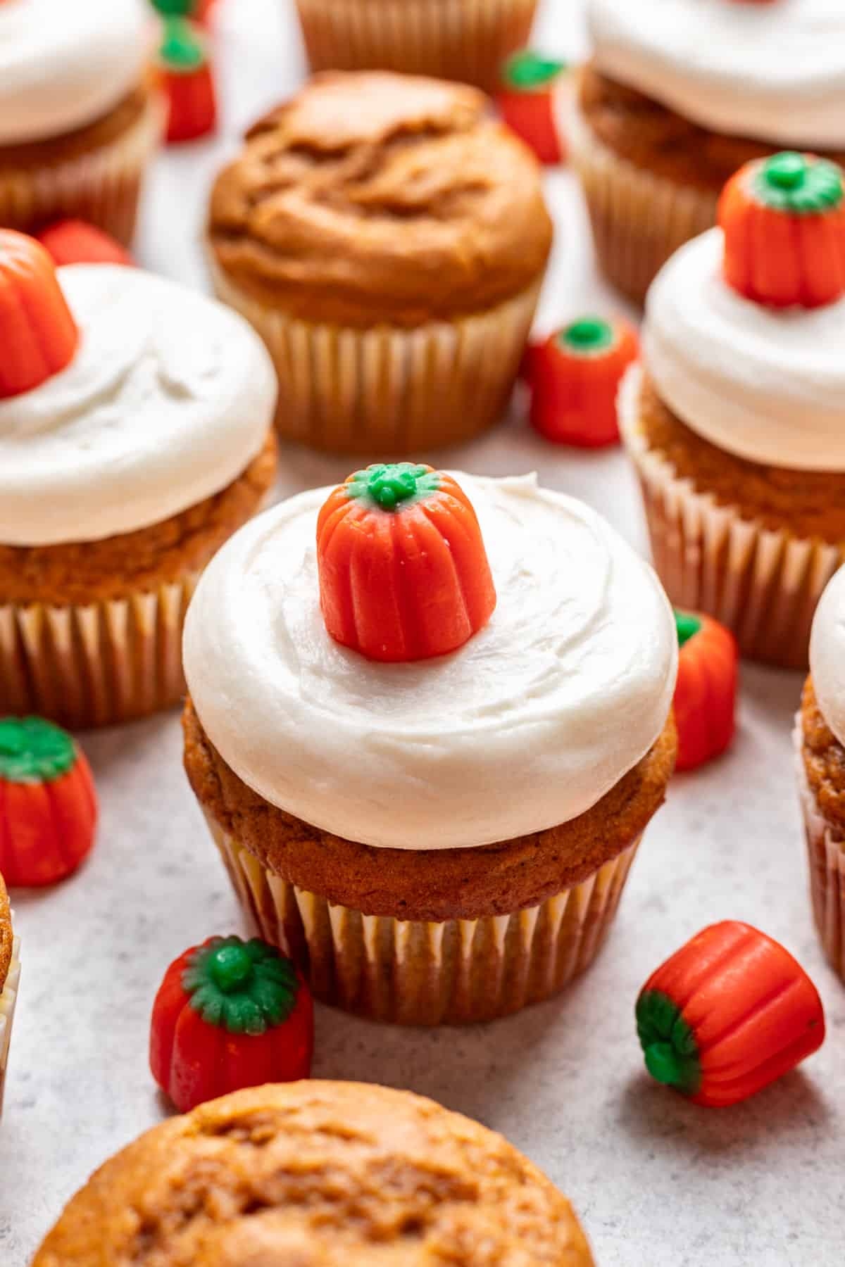 Pumpkin cupcake with cream cheese frosting topped with a candy pumpkin next to more candy pumpkins.