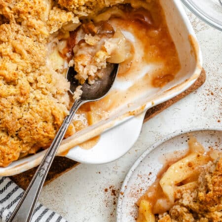 A dish of apple cobbler with some missing and a silver spoon in it.