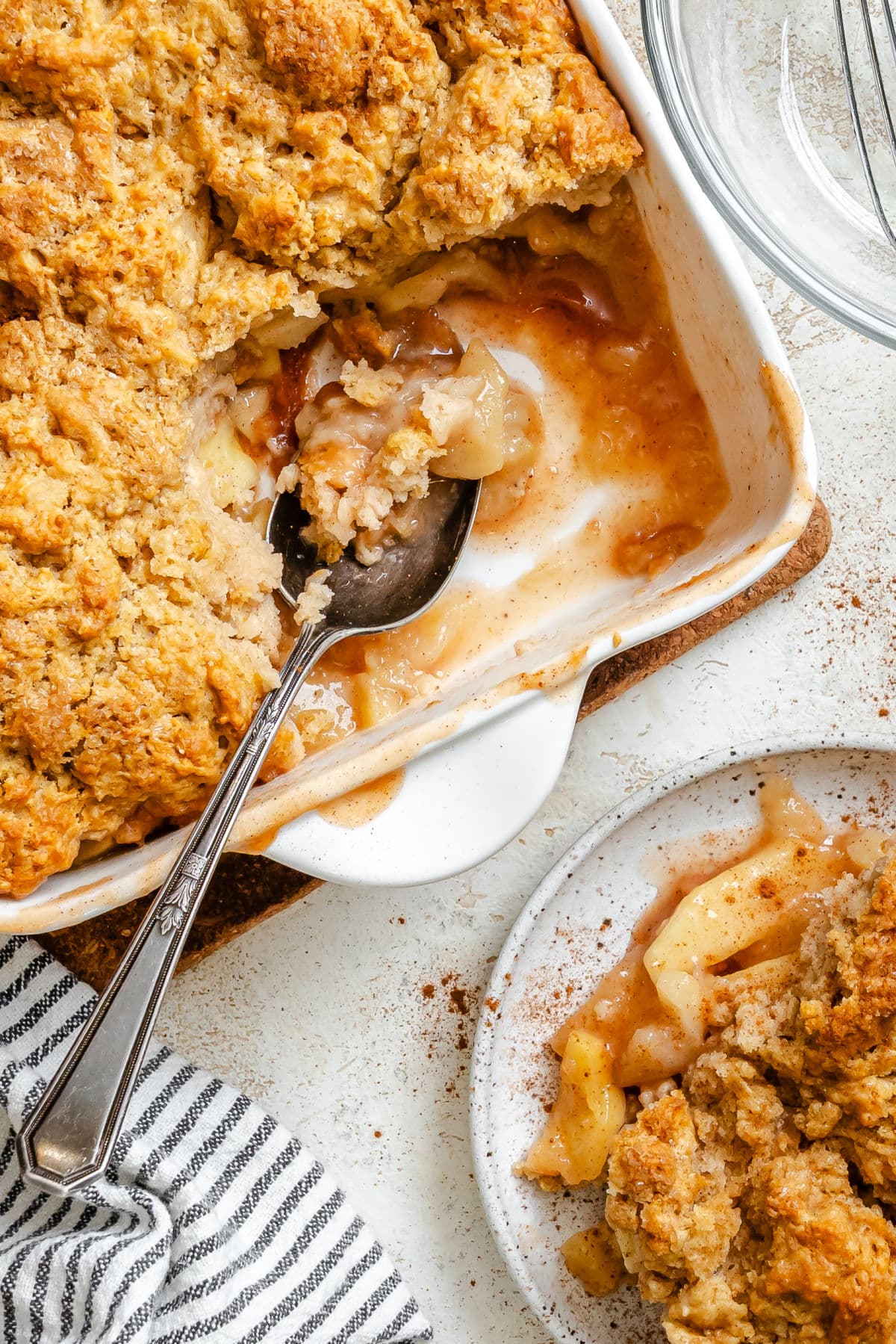 A dish of apple cobbler with some missing and a silver spoon in it.