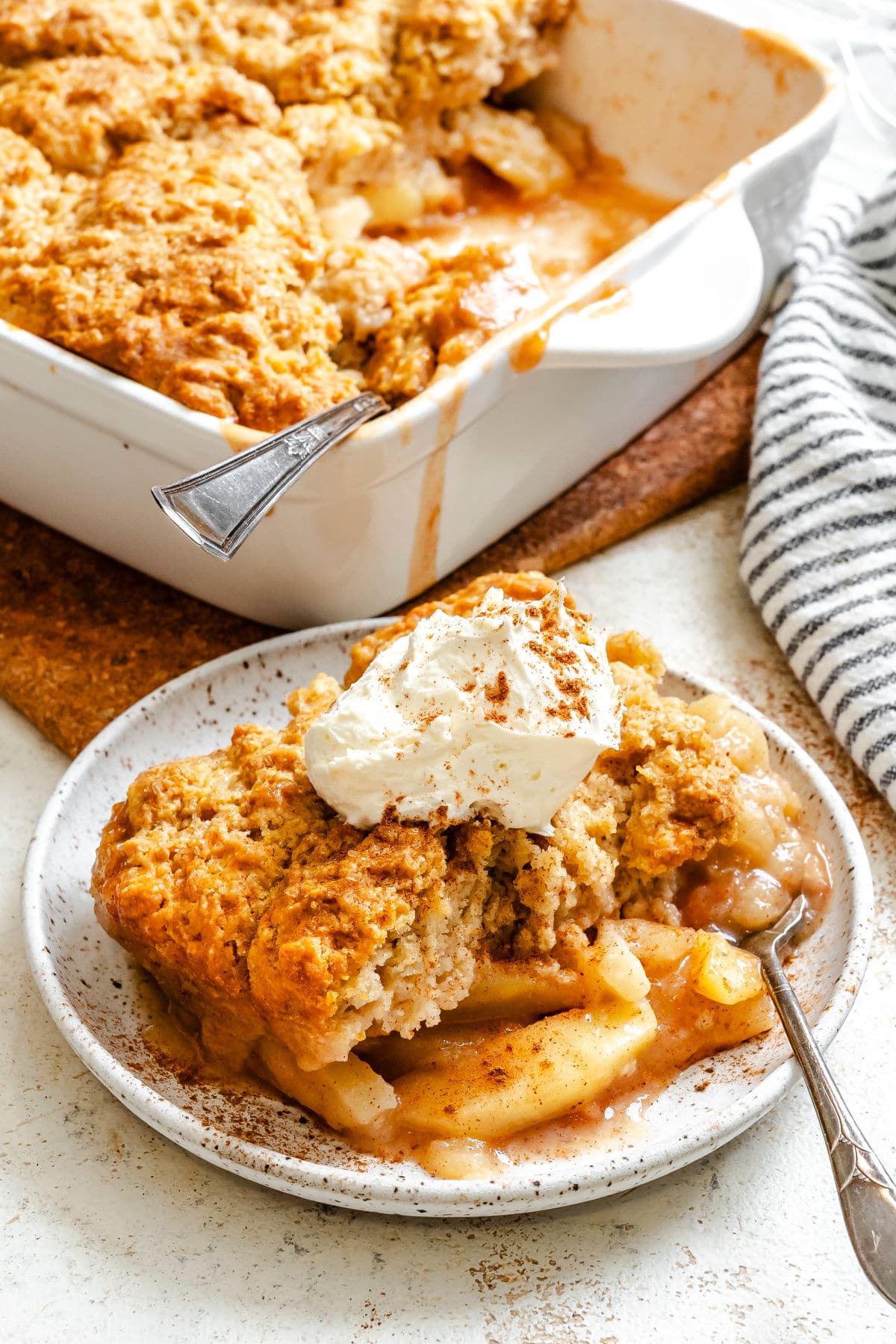 A plate of apple cobbler topped with whipped cream with a silver fork in it. 