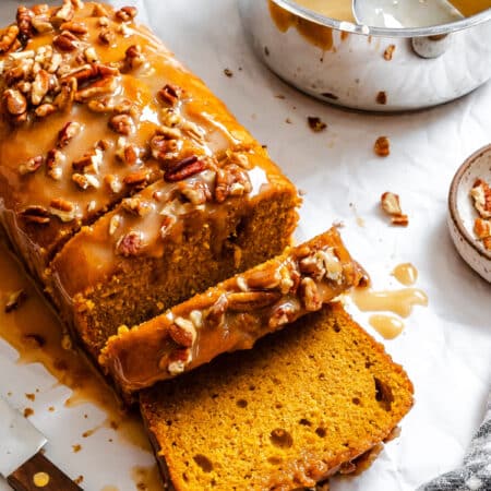 A partially sliced loaf of sweet potato pie bread next to the pot of glaze.