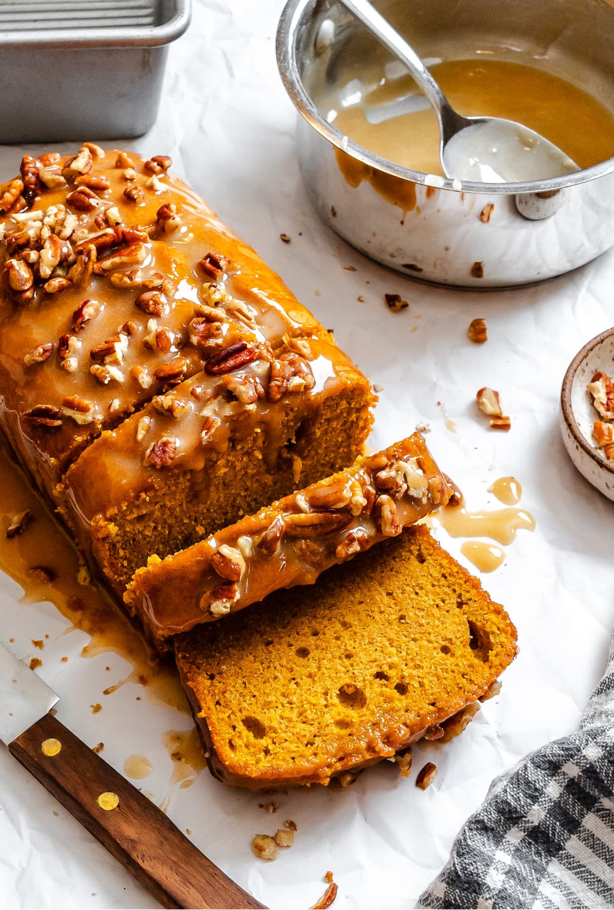 A partially sliced loaf of sweet potato pie bread next to the pot of glaze.