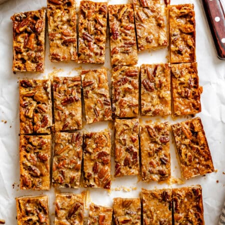 A cut pan of toffee pecan pie bars on a piece of white parchment next to the knife and pan.