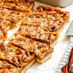 Sliced toffee pecan pie bars on a piece of parchment paper next to the pan.