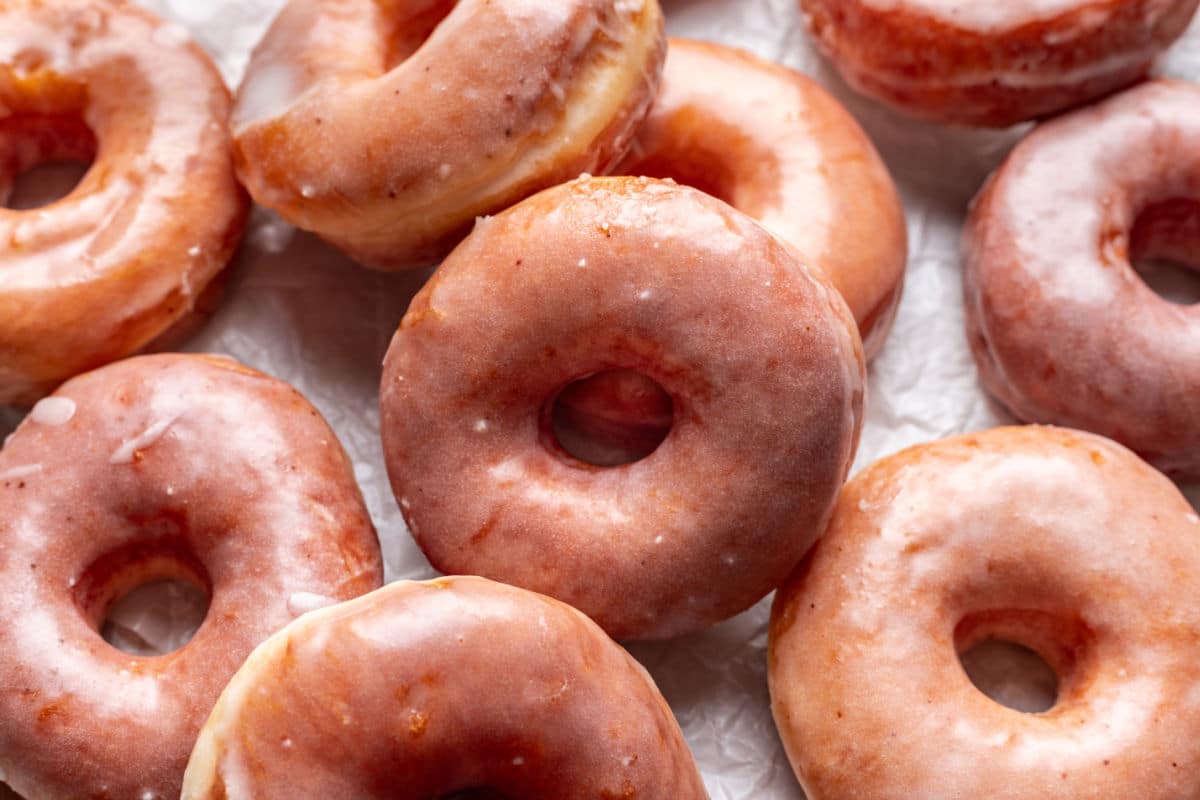 Des donuts à la levure glacés se chevauchant sur du papier sulfurisé blanc.