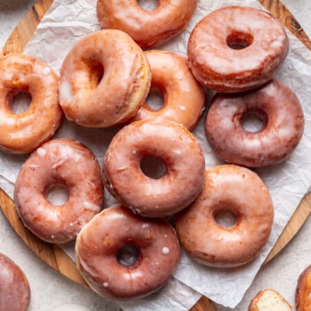 Overlapping yeast doughnuts on a round cutting board lined with parchment paper