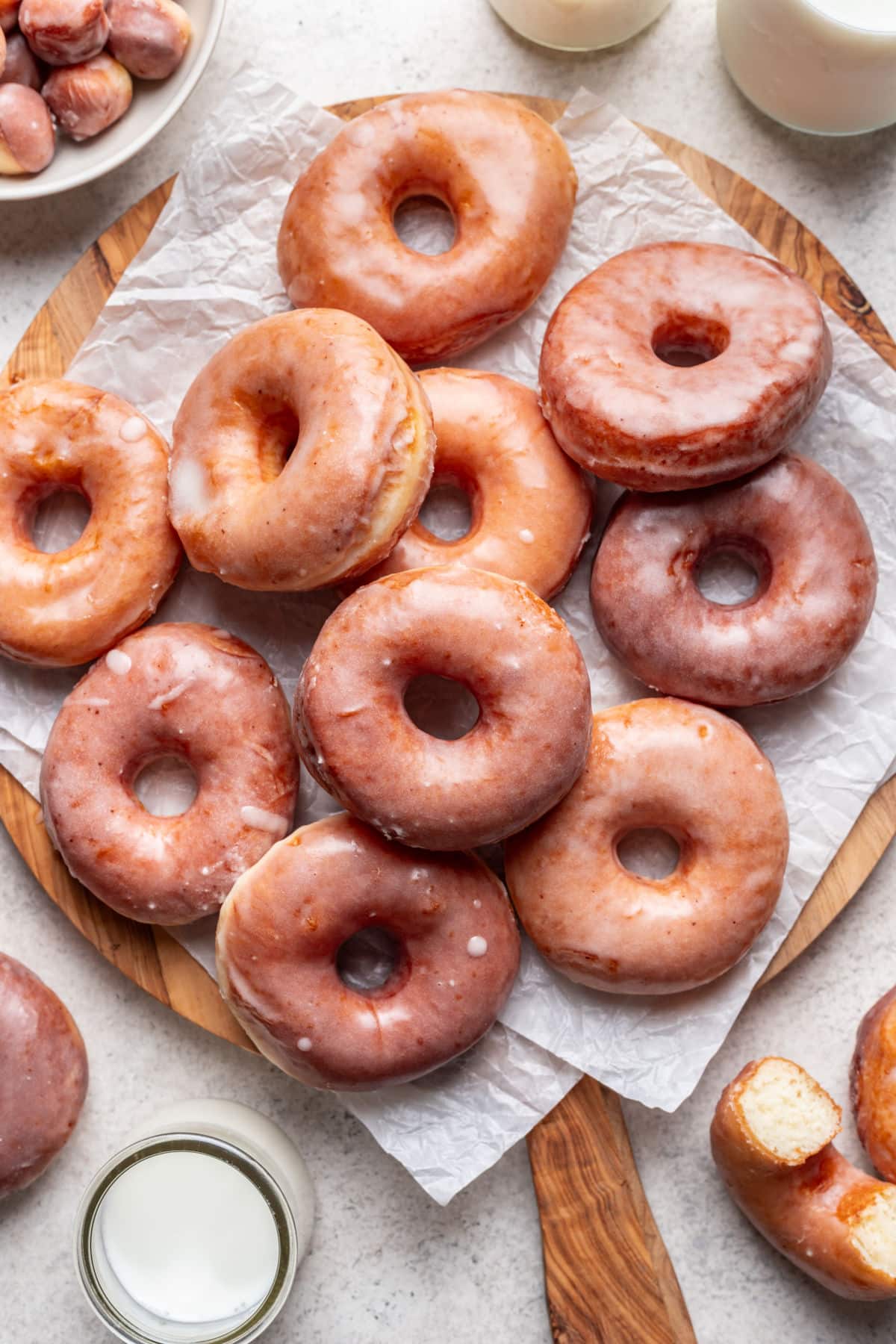 Overlapping yeast doughnuts on a round cutting board lined with parchment paper