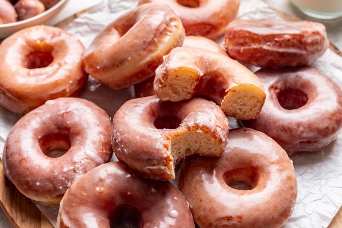 Half a glazed doughnut on top of a doughnut with a bite missing in an overlapping stack of doughnuts.