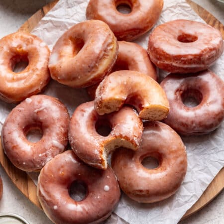 Overlapping glazed yeast donuts on a parchment covered cutting board.